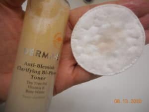 Anti-Blemish Clarifying Bi-Phase Toner. Toner on a cotton pad with the bottle in hand.