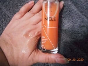 side of Mele skincare EVEN Dark Spot Control Serum bottle next to my hand. A few drops of serum on my hand.