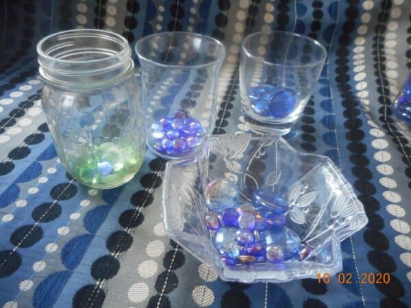 green and blue glass stones in glassware. mason jar, cups and a glass dish.