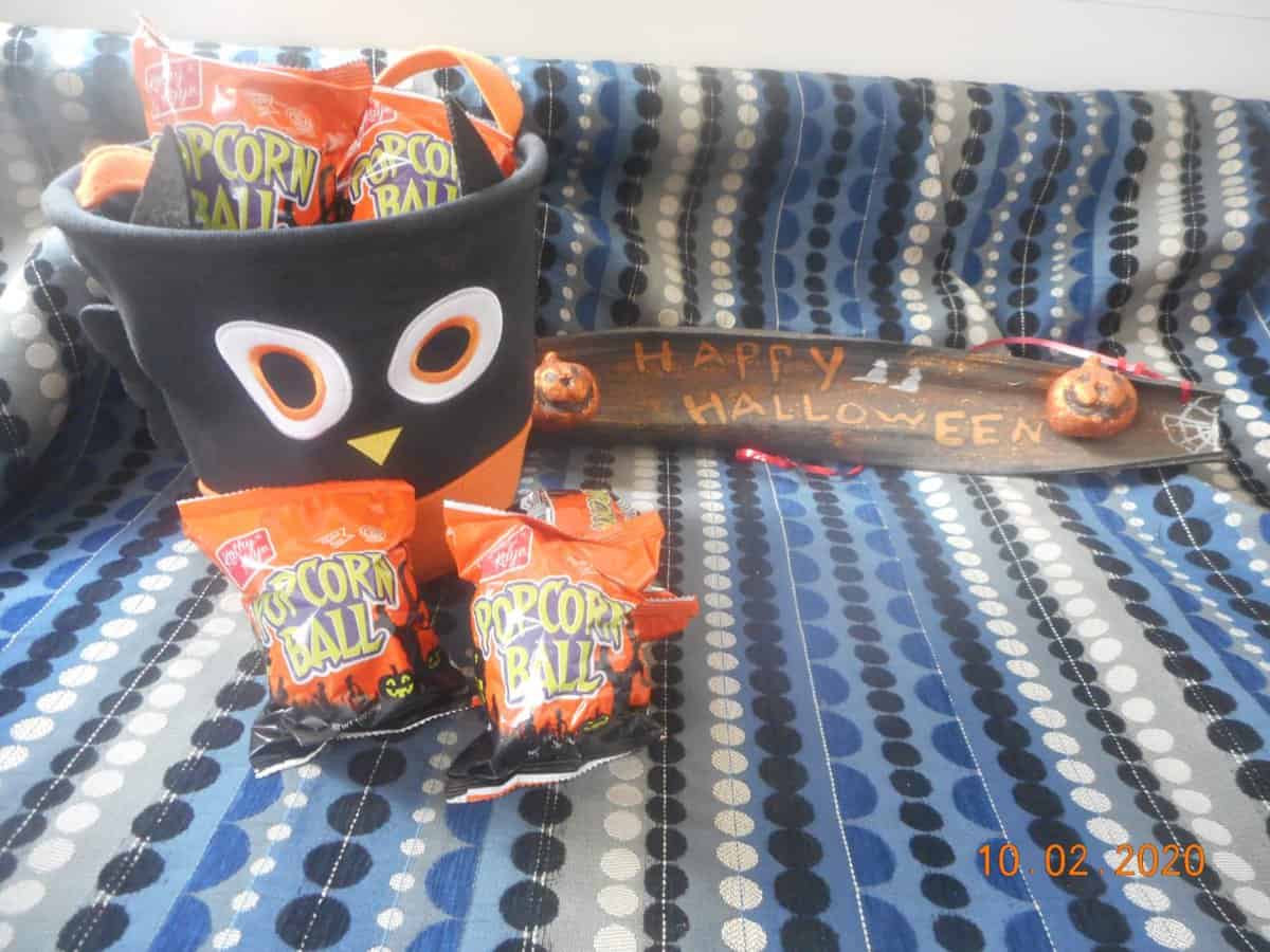 kathy kaye foods popcorn balls packs in front of an owel bucket. A few inside the owl bucket. Happy Halloween sign off to the right.