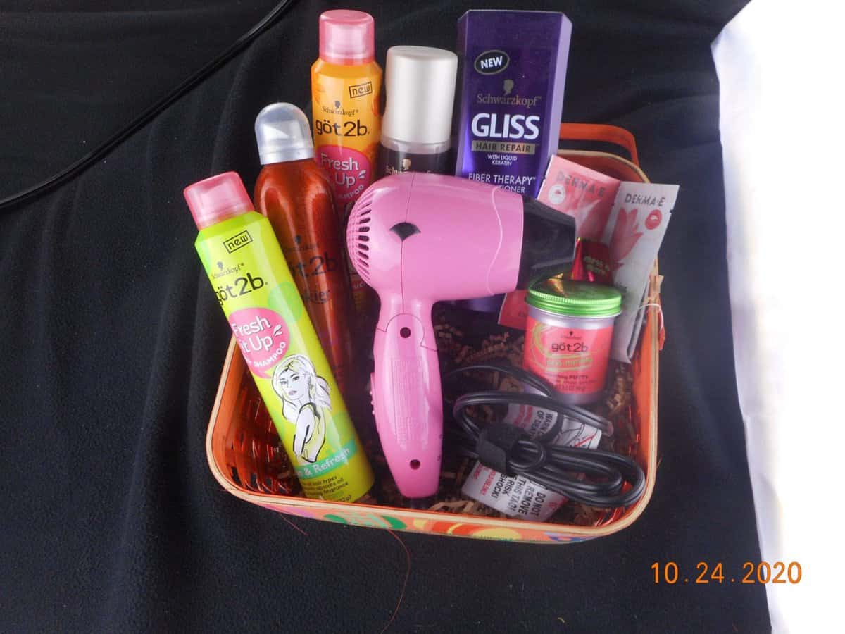 basket filled with hair care products. dry shampoo bottles, conditioner, small hair dryer.