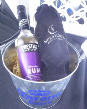 a Corona beer bucket filled with crinkle paper. Also holding a bottle of rum and a bag containing a cocktail shaker.