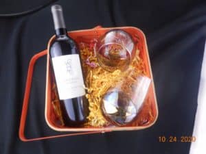 Basket filled with colored crinkle paper. Also contains a bottle of wine and two stemless wine glasses.