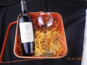 Basket filled with colored crinkle paper. Also contains a bottle of wine and a single wine glass.