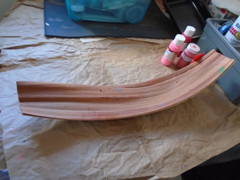 palm bark with pre-drilled holes next to a few acyclic paints. pants are red and pinks.