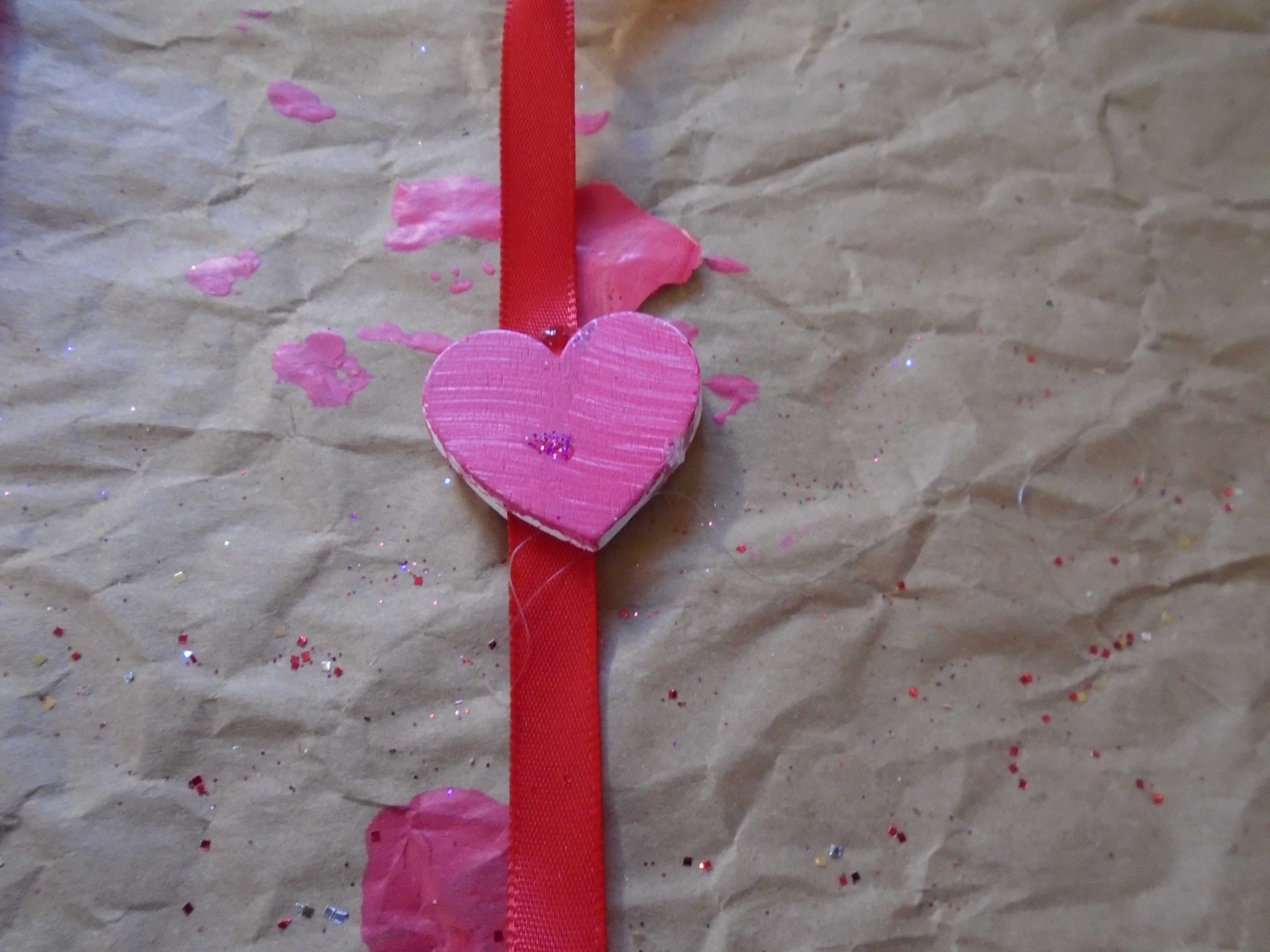 close up of heart glued to ribbon. pink heart on red ribbon.