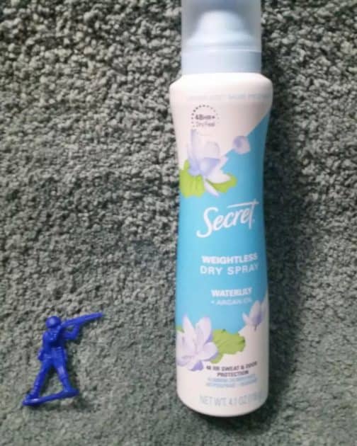 blue army man toy with a bottle of Secret weightless dray deodorant spray in scent white lily plus argan oil.