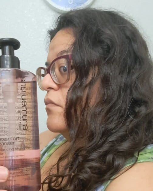 delicate comfort deep cleanser by shu Uemura clarifying shampoo bottle in my hand with a side view of my hair.