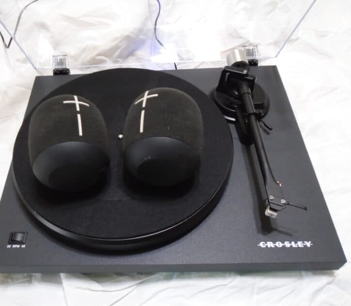 2 black with white bluetooth speakers (Ultimate ears wonderboom) lying on a crosley turntable.