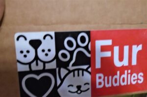 Furbuddies logo on a box. black white and red sticker with a dog face, cat face, paws and a heart. Withe text reading fur buddies.