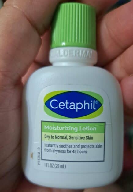 Travel size Cetaphil moisturizing loiton in my (V) hand. White bottle with green lid. Label is blue, green and white.