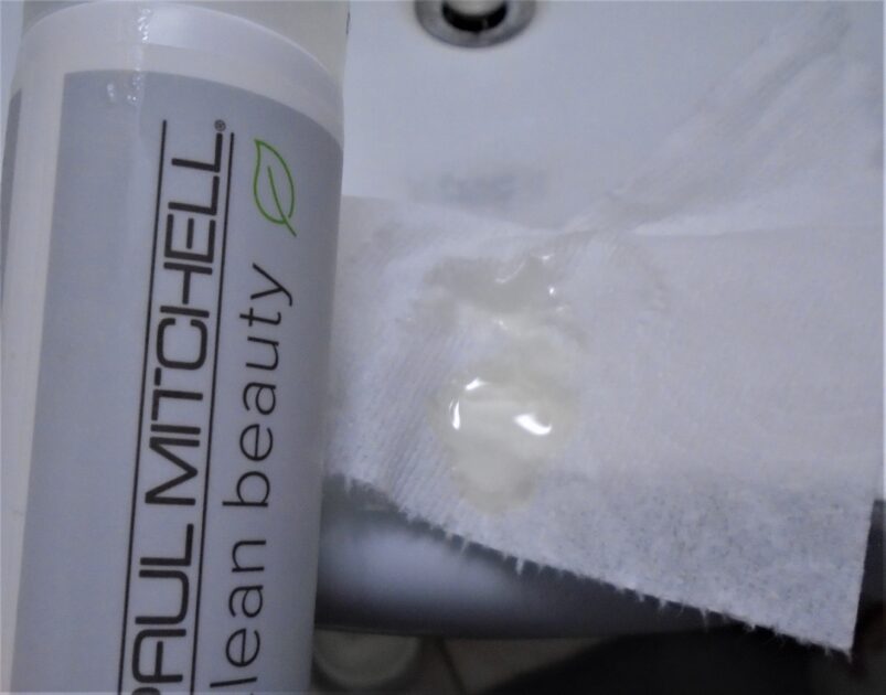 Paul Mitchell Clean Beauty shampoo on some tissue. The shampoo is a whitish shade. Bottle next to the shampoo.Clean Beauty Scalp Therapy Shampoo.