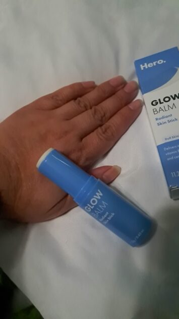 Hero Cosmetics Glow Balm in box. with Glow balm stick resting on my (V) hand.