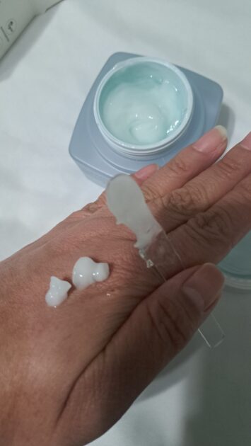 Some of the face shop the therapy vegan moisture blending cream on V's hand. hoding the spatula and open jar in the image.